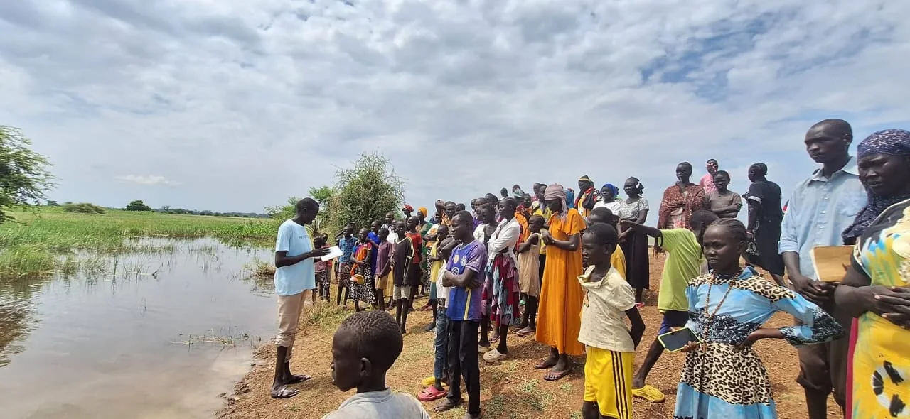 Community members gathered outdoors near a waterway for a ministry activity